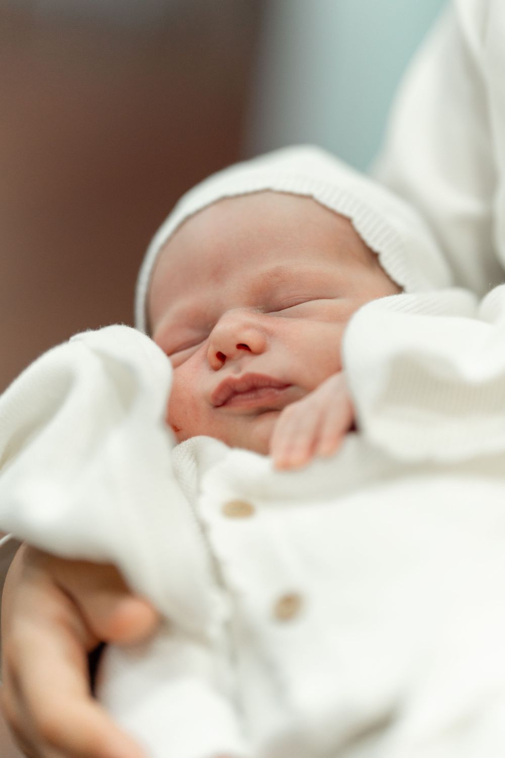 Sleeping newborn baby wrapped in white clothing with a knit cap.