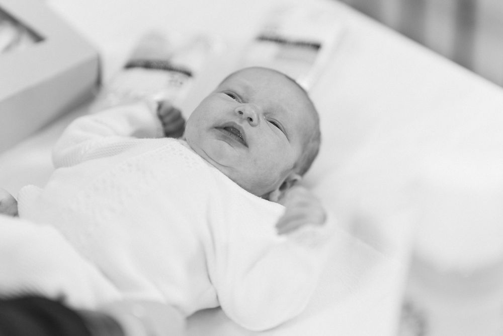 A sleeping newborn baby in white clothing on white bedding in black and white.