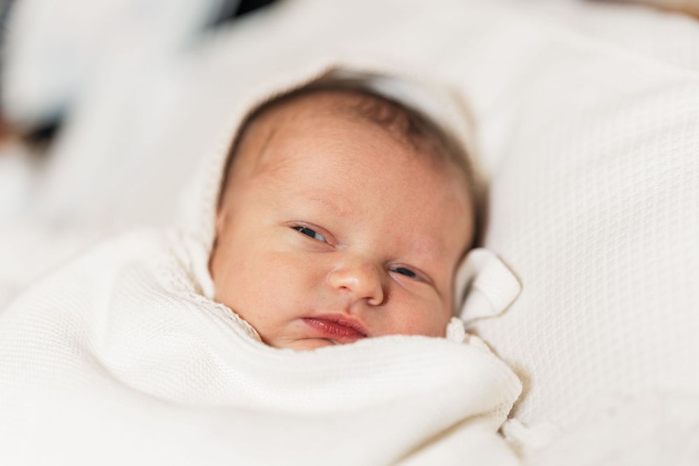 Newborn baby wrapped in white blanket with peaceful expression.
