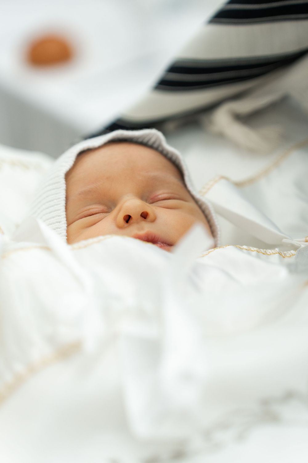 Close up of a sleeping baby's face wrapped in white with a soft knit cap.