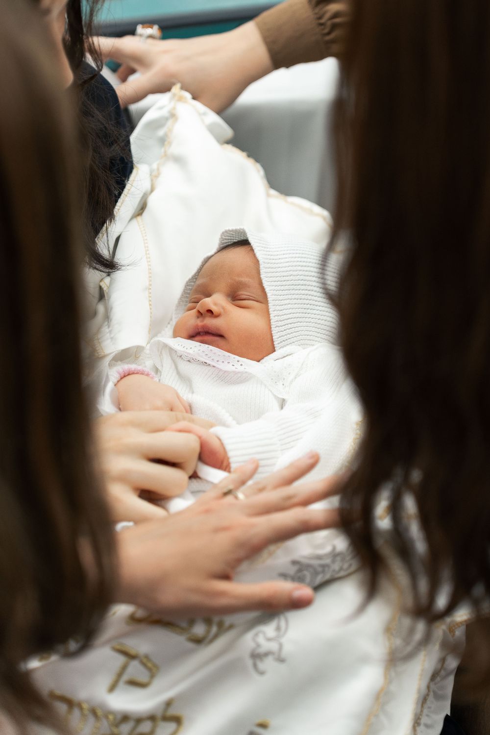 A sleeping newborn baby wearing white being cradled by gentle hands.