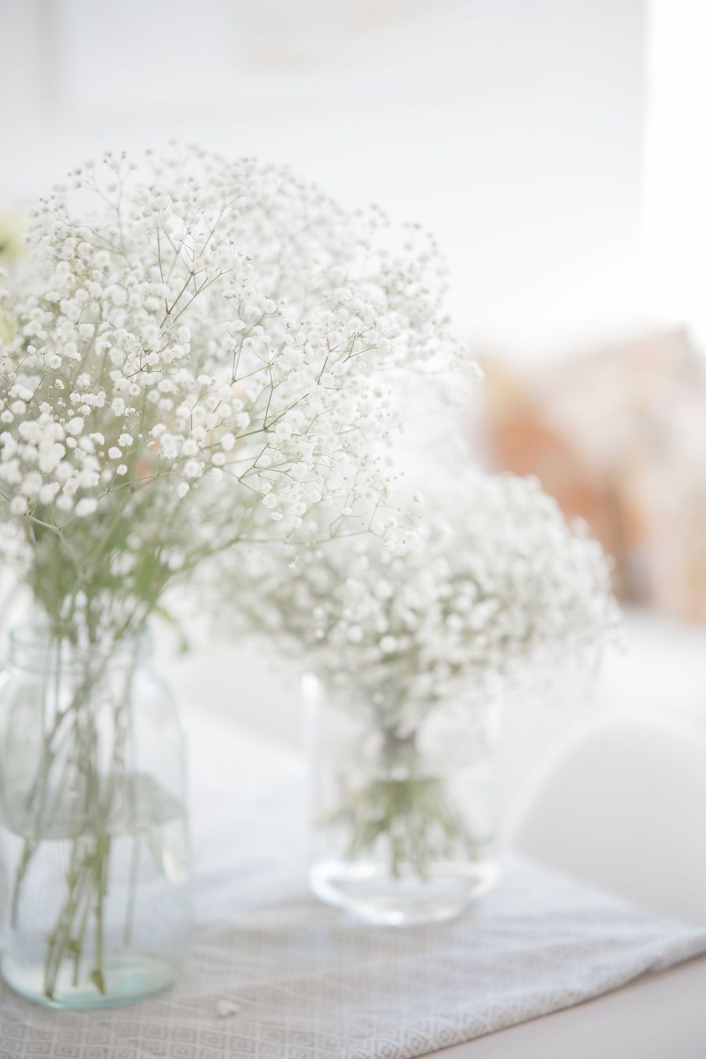 Delicate white baby's breath flowers arranged in clear glass vases on a linen cloth, perfect for weddings.