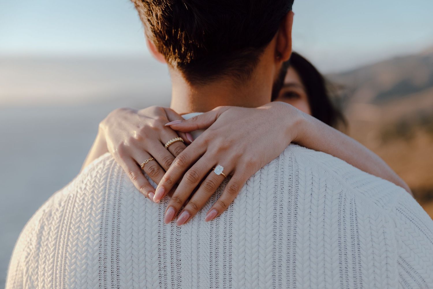 Close-up shot of hands embracing around shoulders against a mountain backdrop.