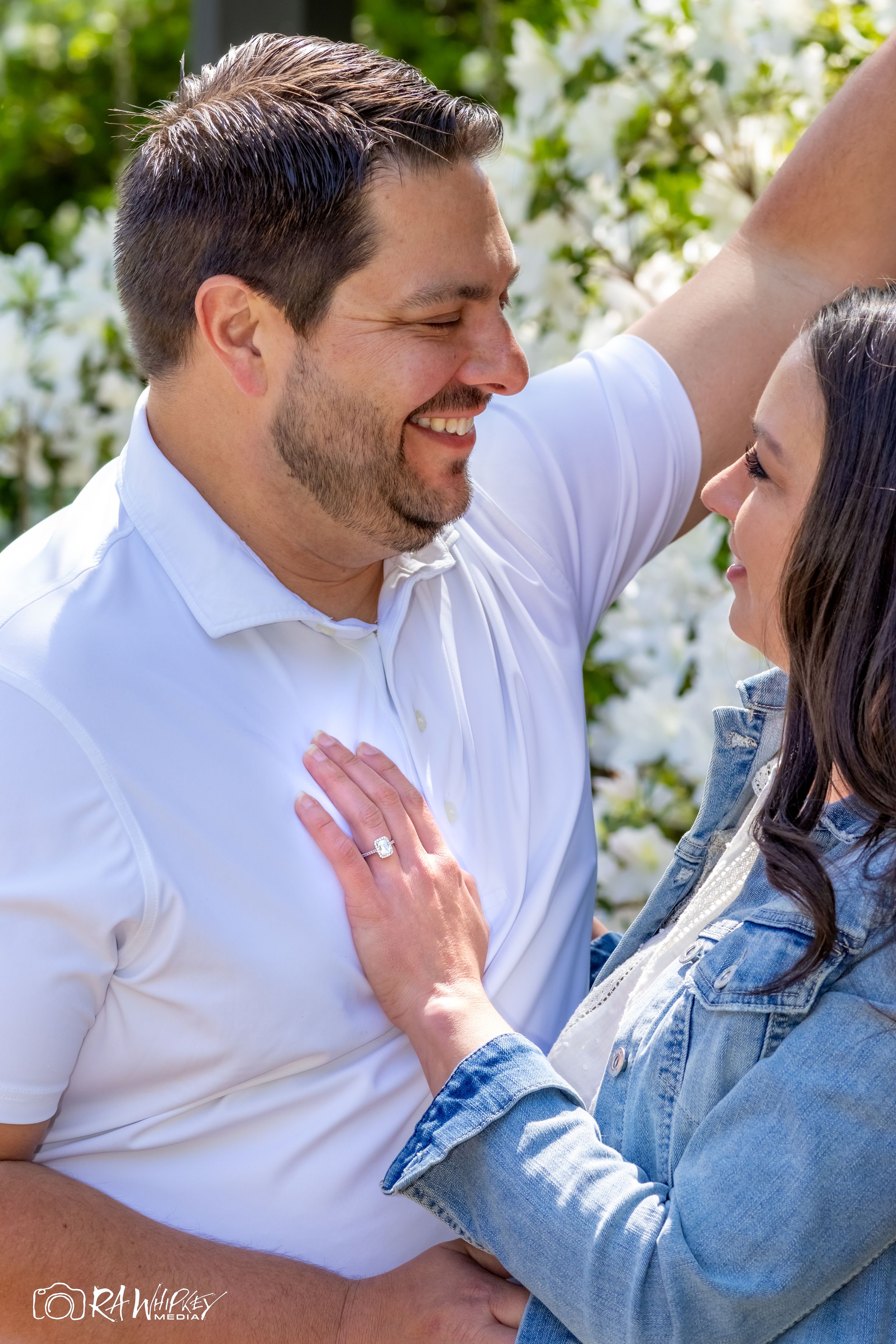 An intimate moment captured between a couple in white and denim against a flowering background.