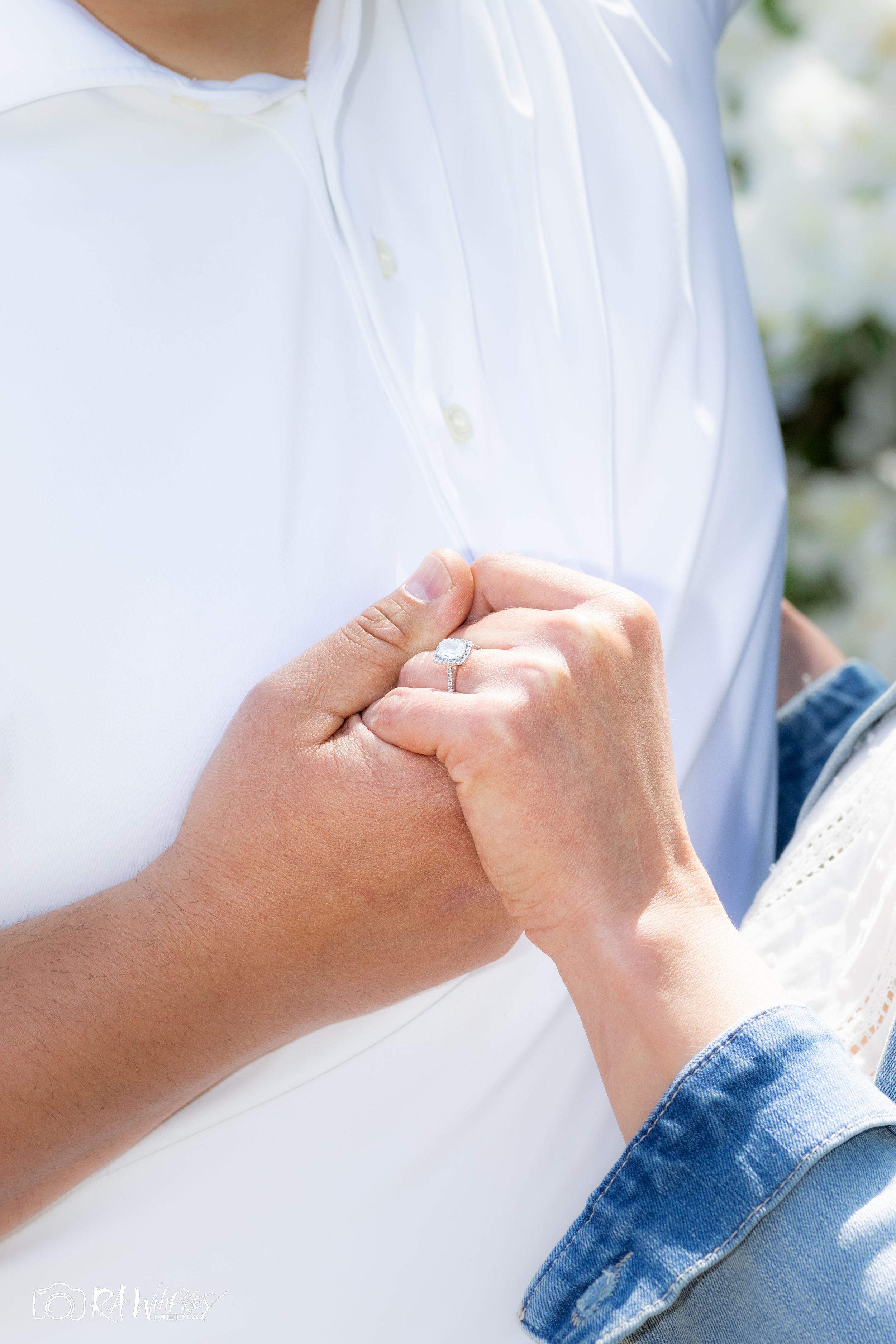 Close-up of clasped hands showing wedding rings against a white and denim outfit.