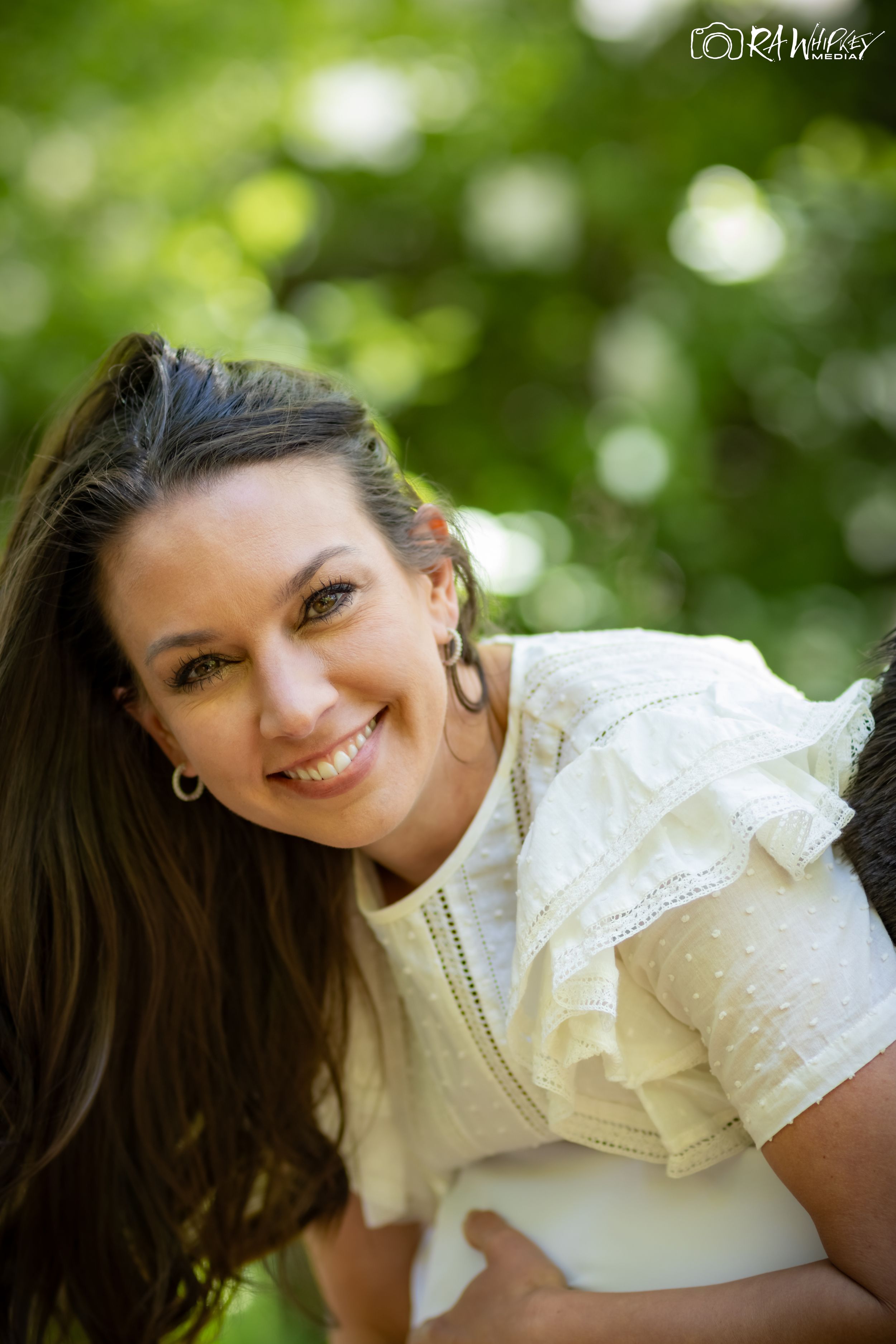 Portrait of a smiling woman in a white dress against a blurred natural background.