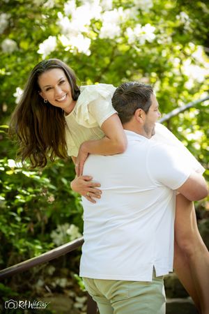 Playful couple wearing white outfits enjoying a piggyback ride outdoors.