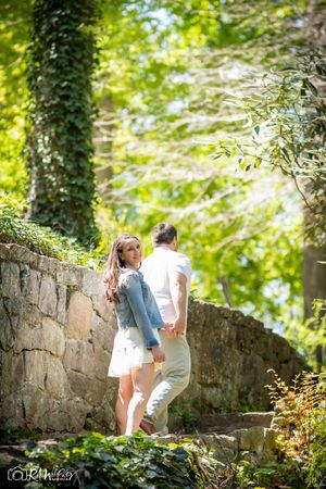 Couple walking up stone steps along an ivy-covered wall in dappled sunlight.