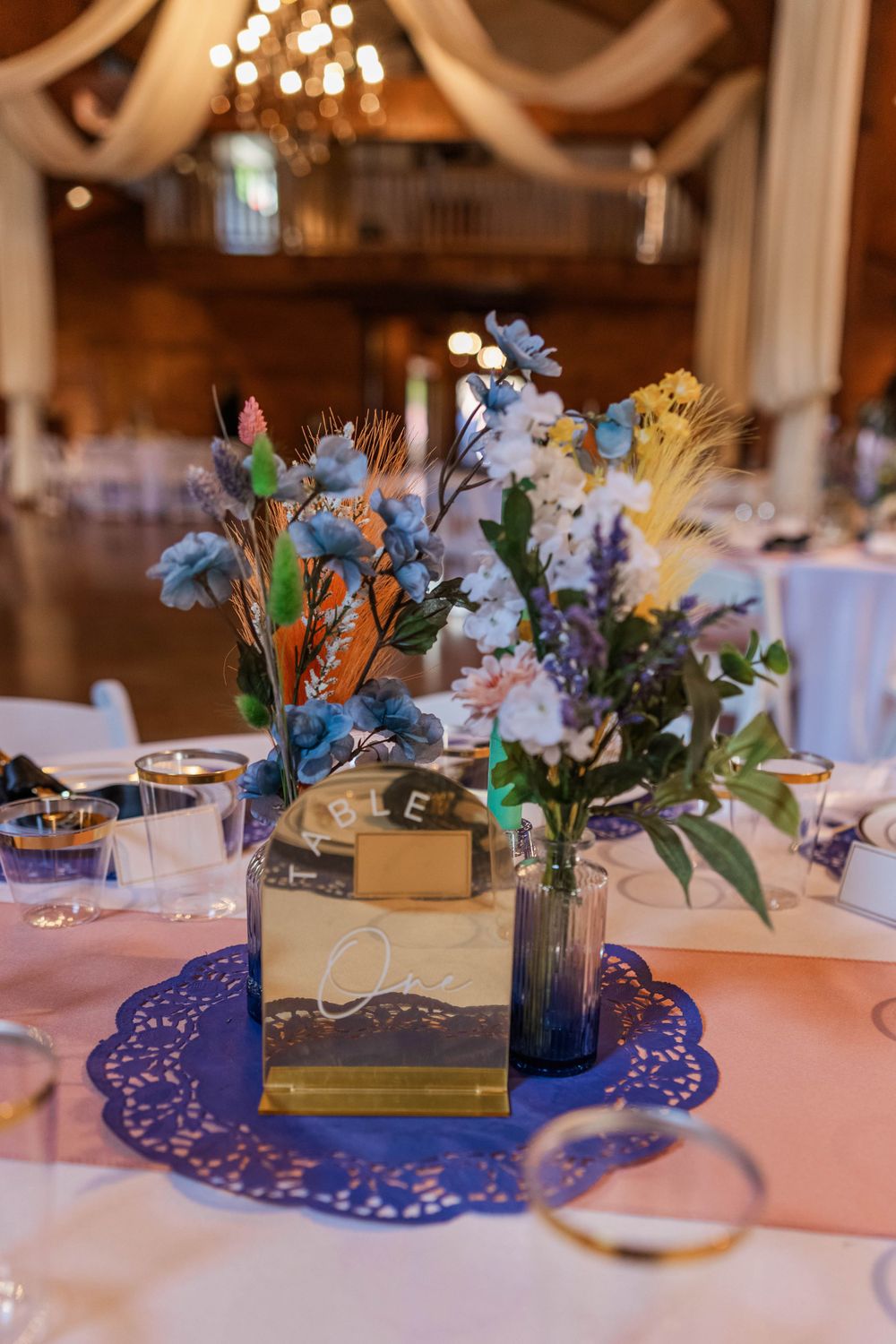 Wedding centerpieces featuring colorful flowers on blue doilies with table numbers.