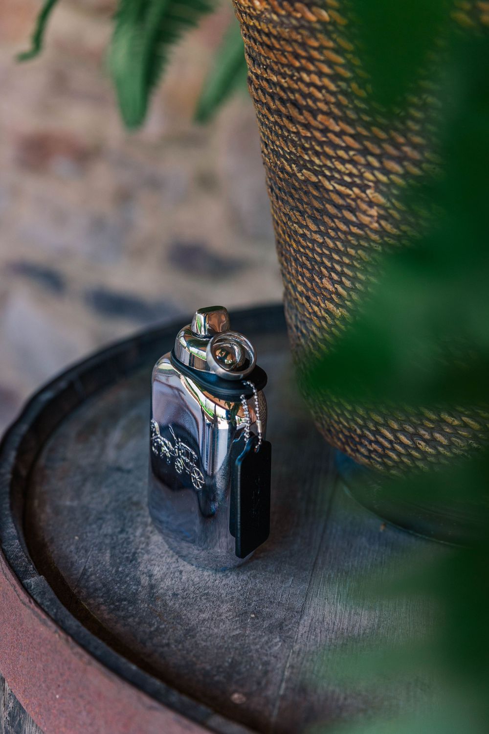A dark metallic lighter sitting on a wooden surface with green foliage in the background.