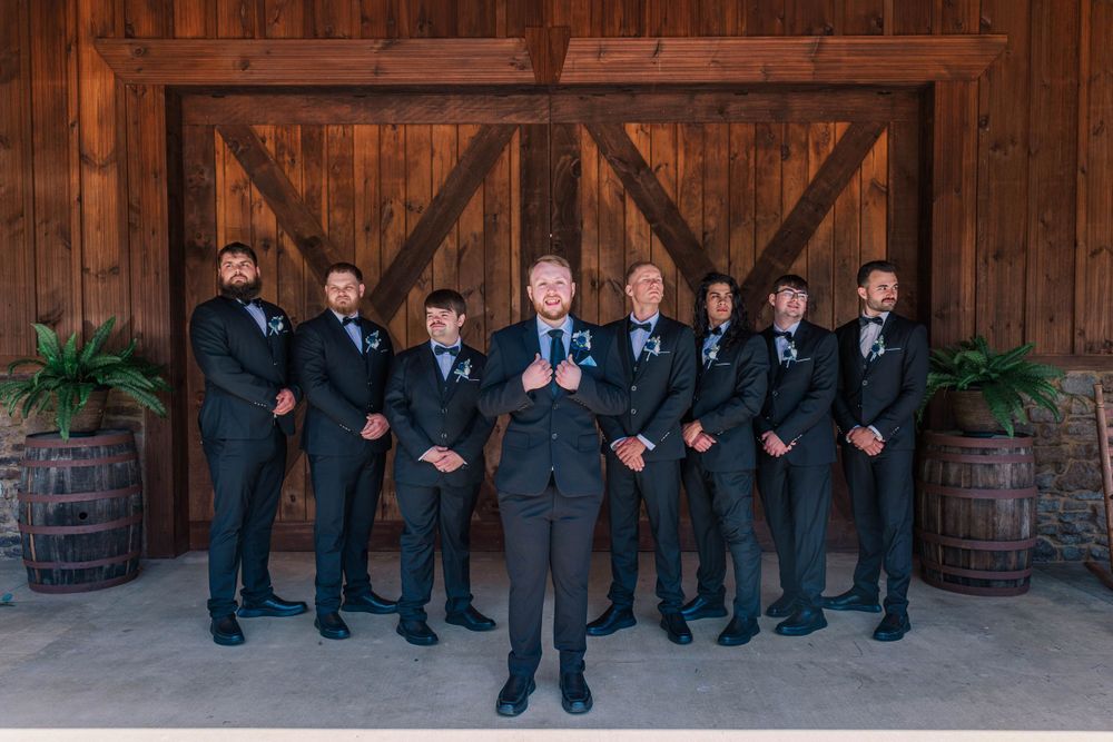 A group of groomsmen in dark suits posed formally in front of a rustic wooden barn door.