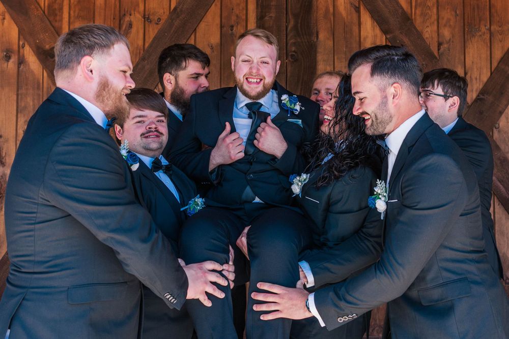 Groomsmen in dark suits playfully lifting someone in a candid moment.