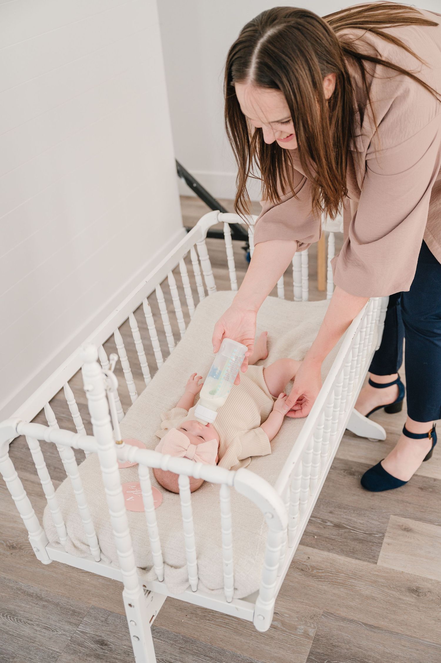 A caretaker tends to a baby laying in a white wooden crib on a hardwood floor.