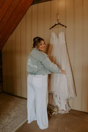 White wedding dress hanging in rustic room with soft natural lighting.