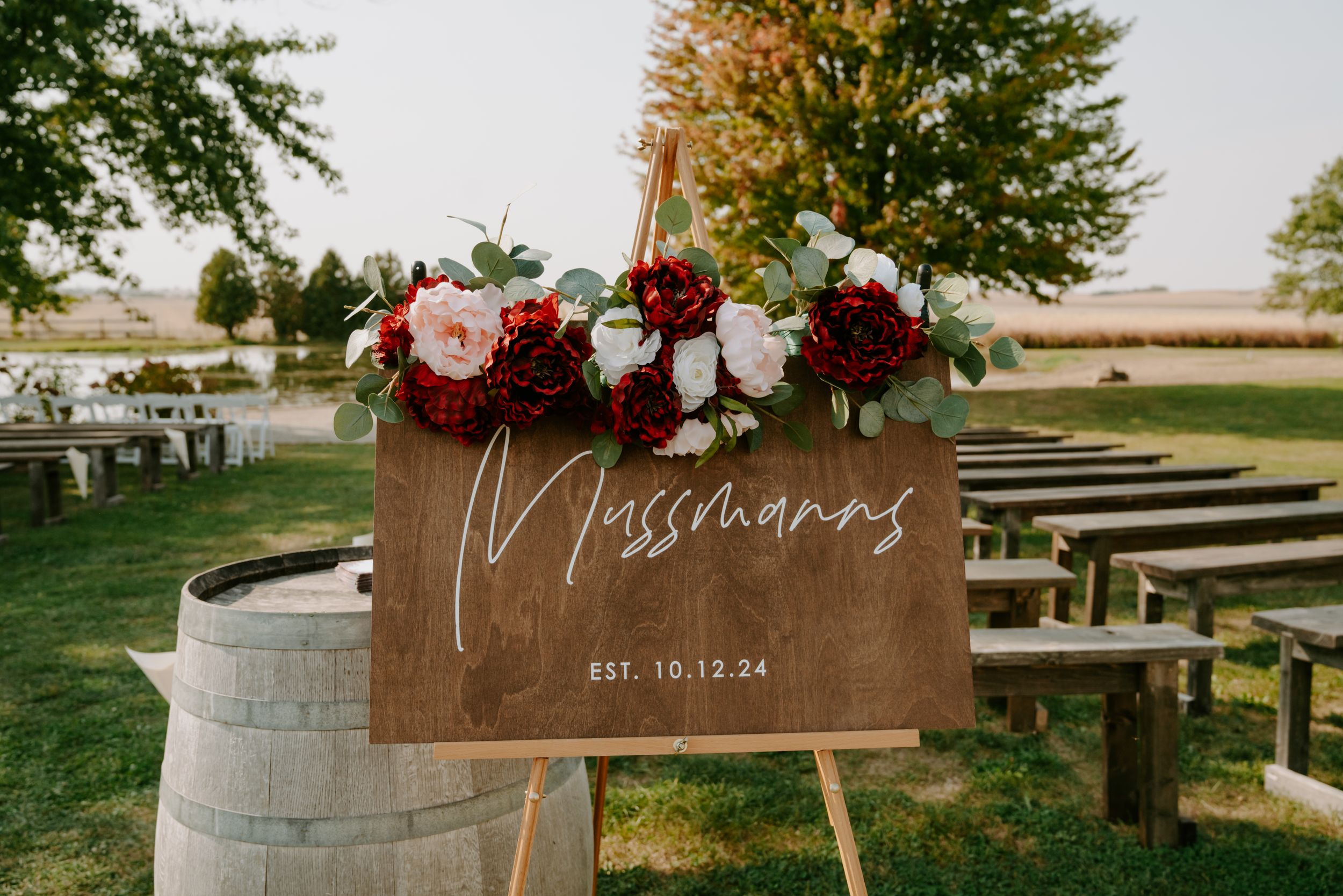 Rustic wooden wedding welcome sign decorated with burgundy flowers and greenery.