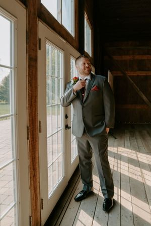 Groomsmen in dark suits looking out large windows in rustic venue.