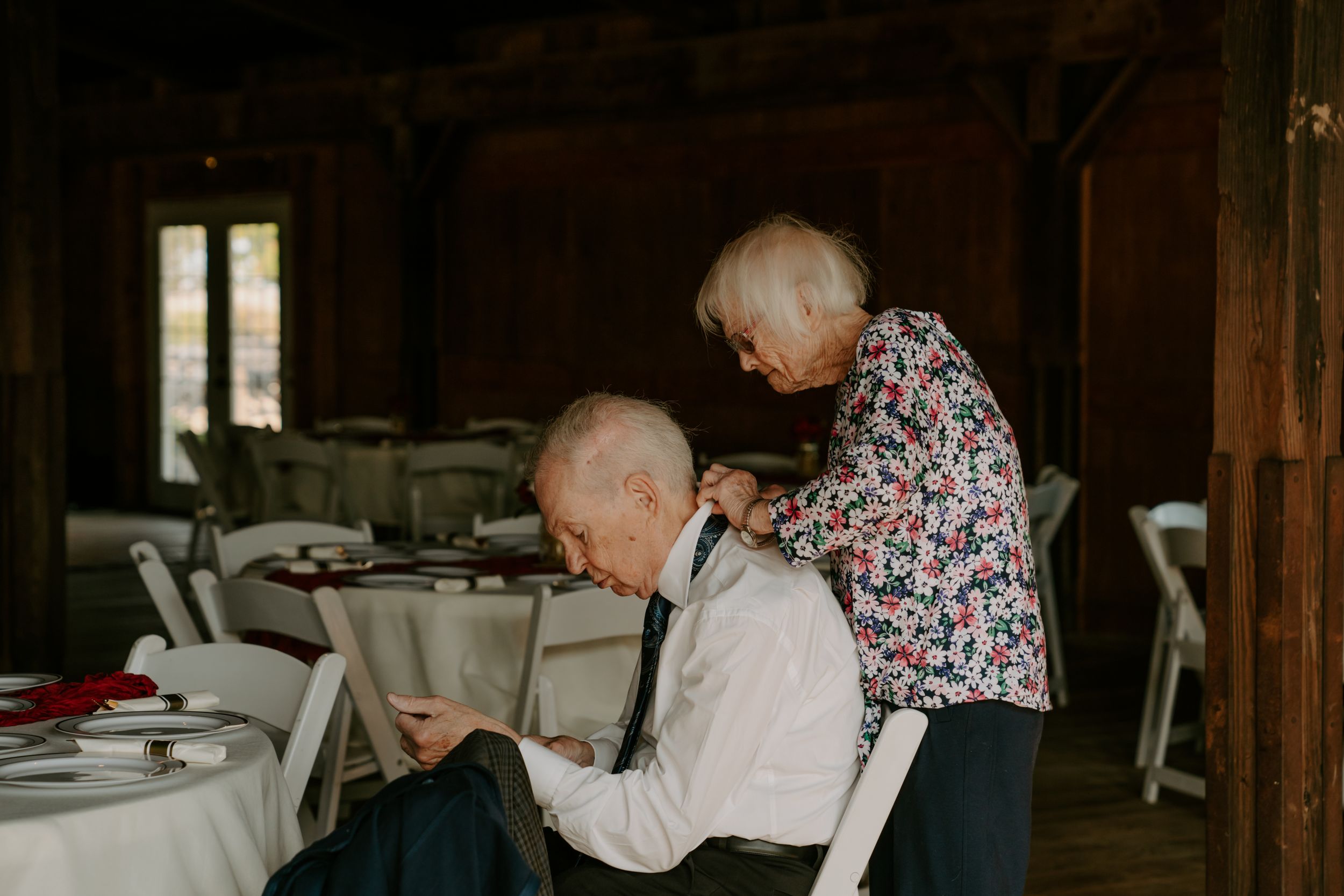 Elderly guests enjoying a meal at tables in a dimly lit rustic venue.