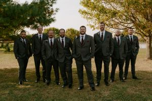 Wedding party in black suits standing in line outdoors during autumn.
