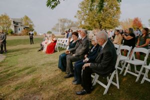 Wedding guests seated in white chairs for outdoor autumn ceremony.