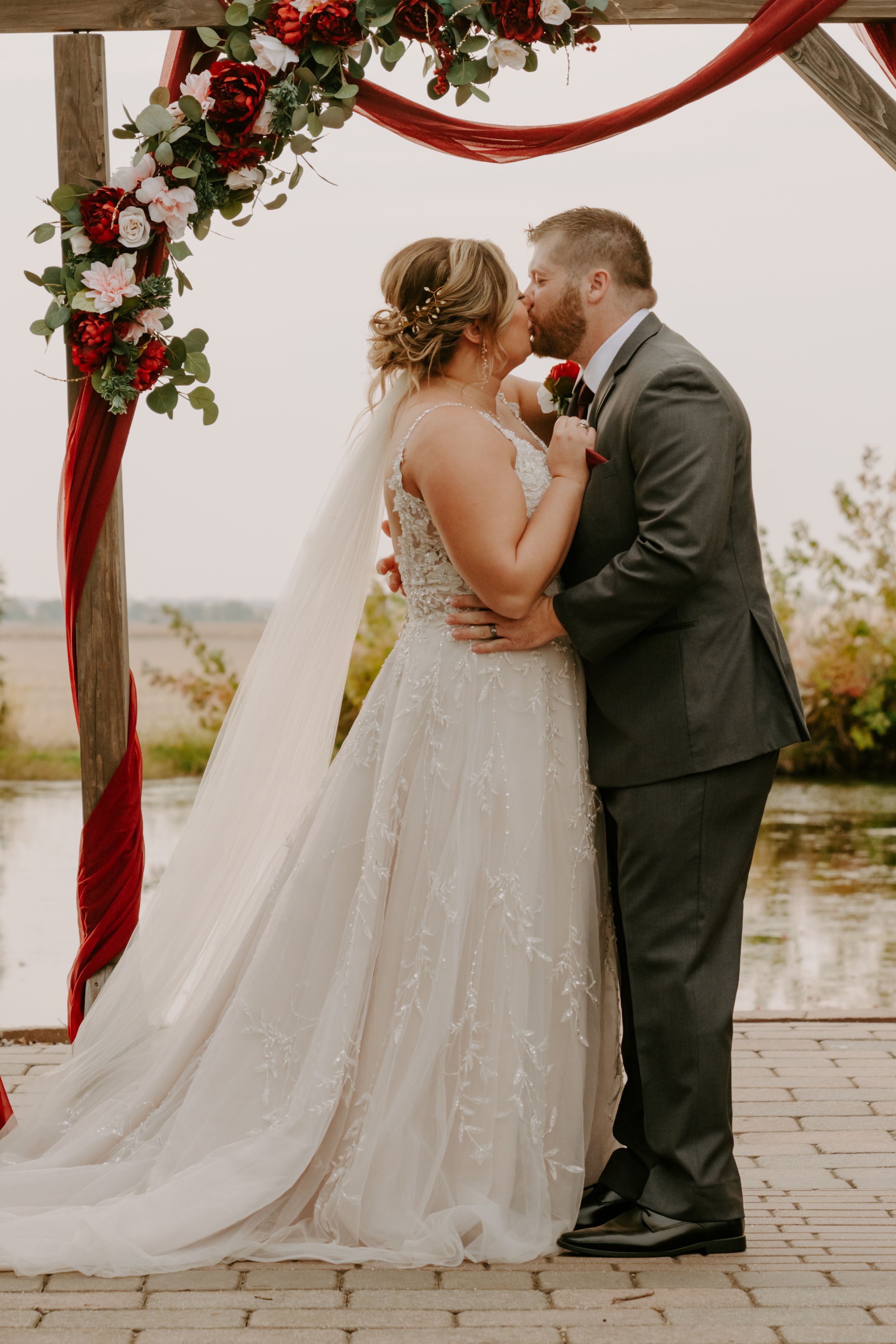 Wedding arch decorated with red fabric and floral arrangements against a scenic backdrop.