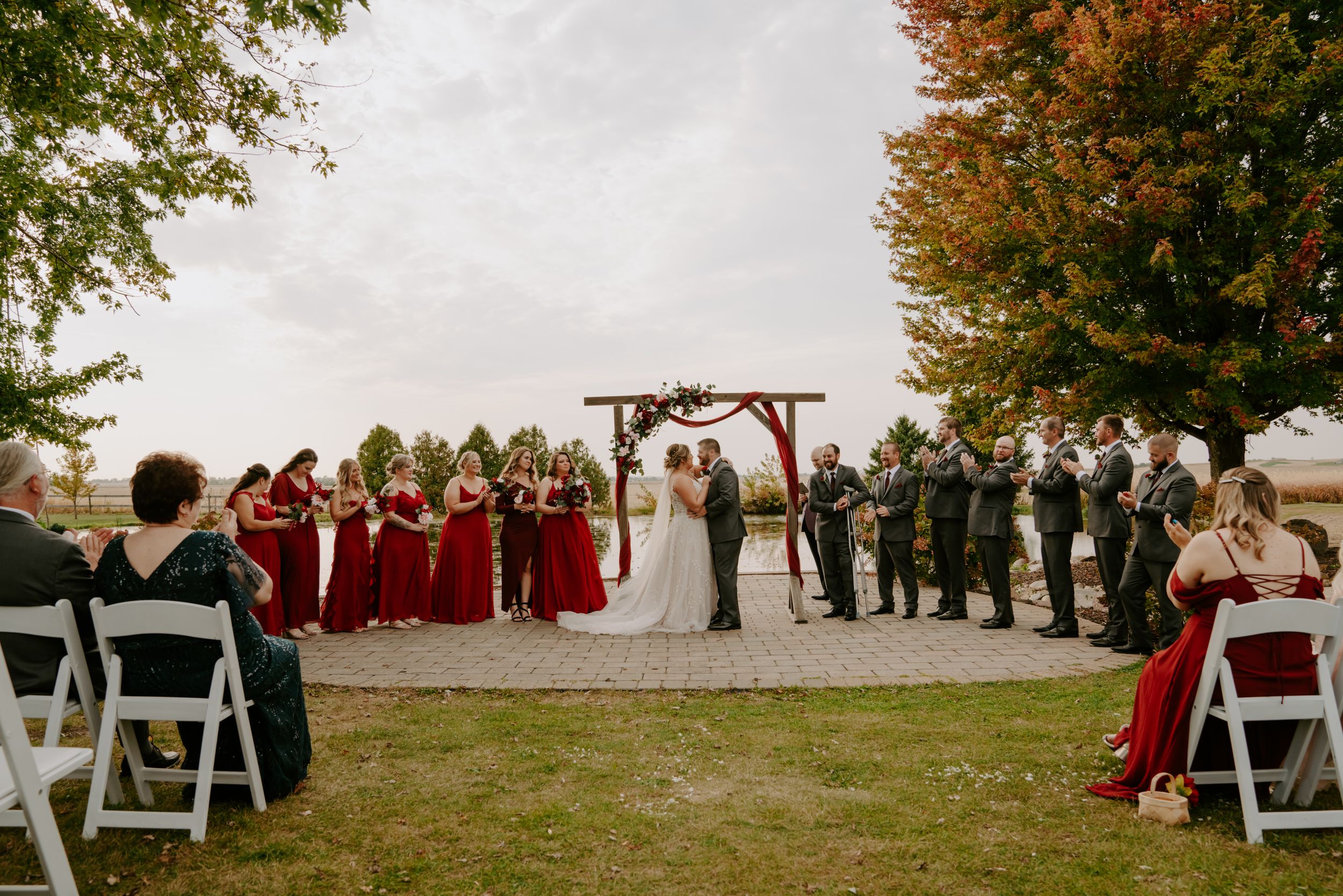 Wedding ceremony setup outdoors with white chairs and fall foliage in the background.
