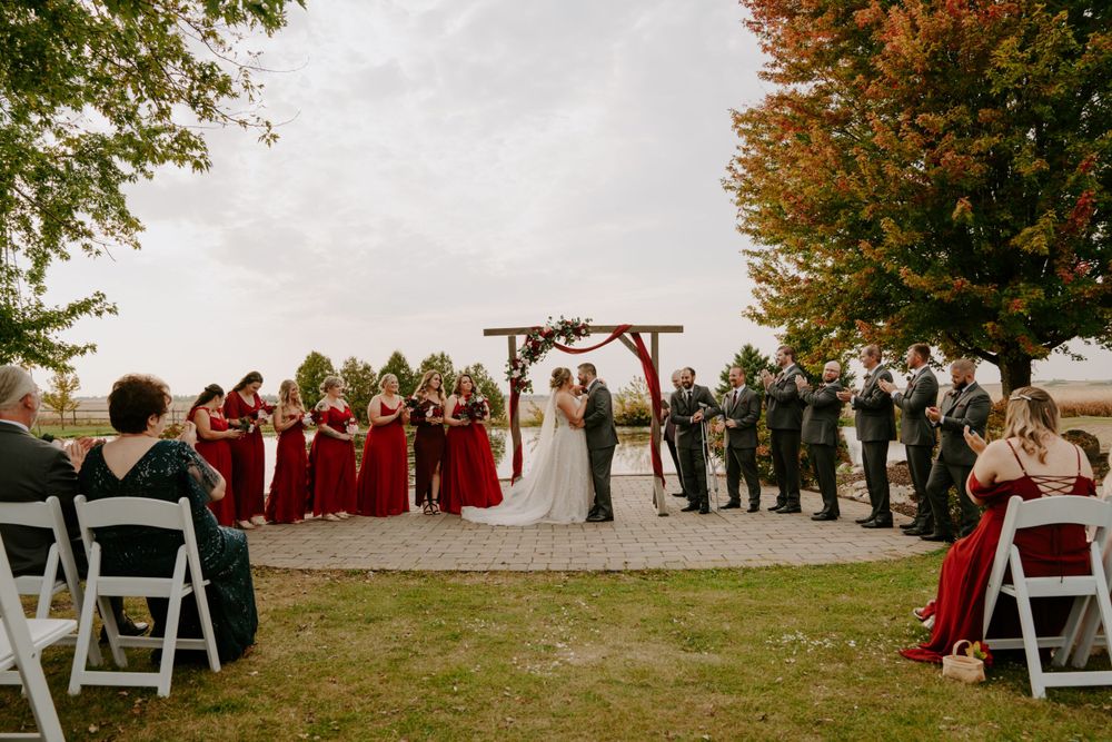 Wedding ceremony setup outdoors with white chairs and fall foliage in the background.