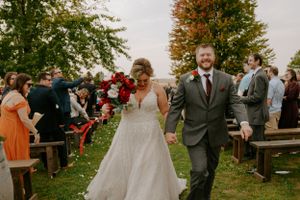 Outdoor wedding celebration with guests seated on rustic benches surrounded by fall trees.