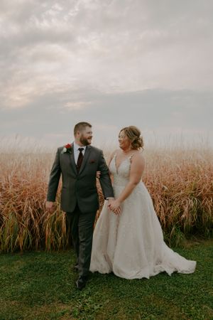 Newlyweds walking together near cornfield during autumn wedding photoshoot.