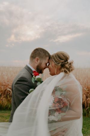 A romantic wedding photoshoot in a golden cornfield at sunset with flowing veil caught in the breeze.