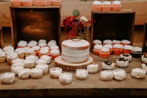 White wedding cupcakes and desserts displayed on a rustic wooden table at a reception.