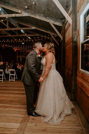 A couple shares their first dance in a rustic barn venue with string lights overhead.