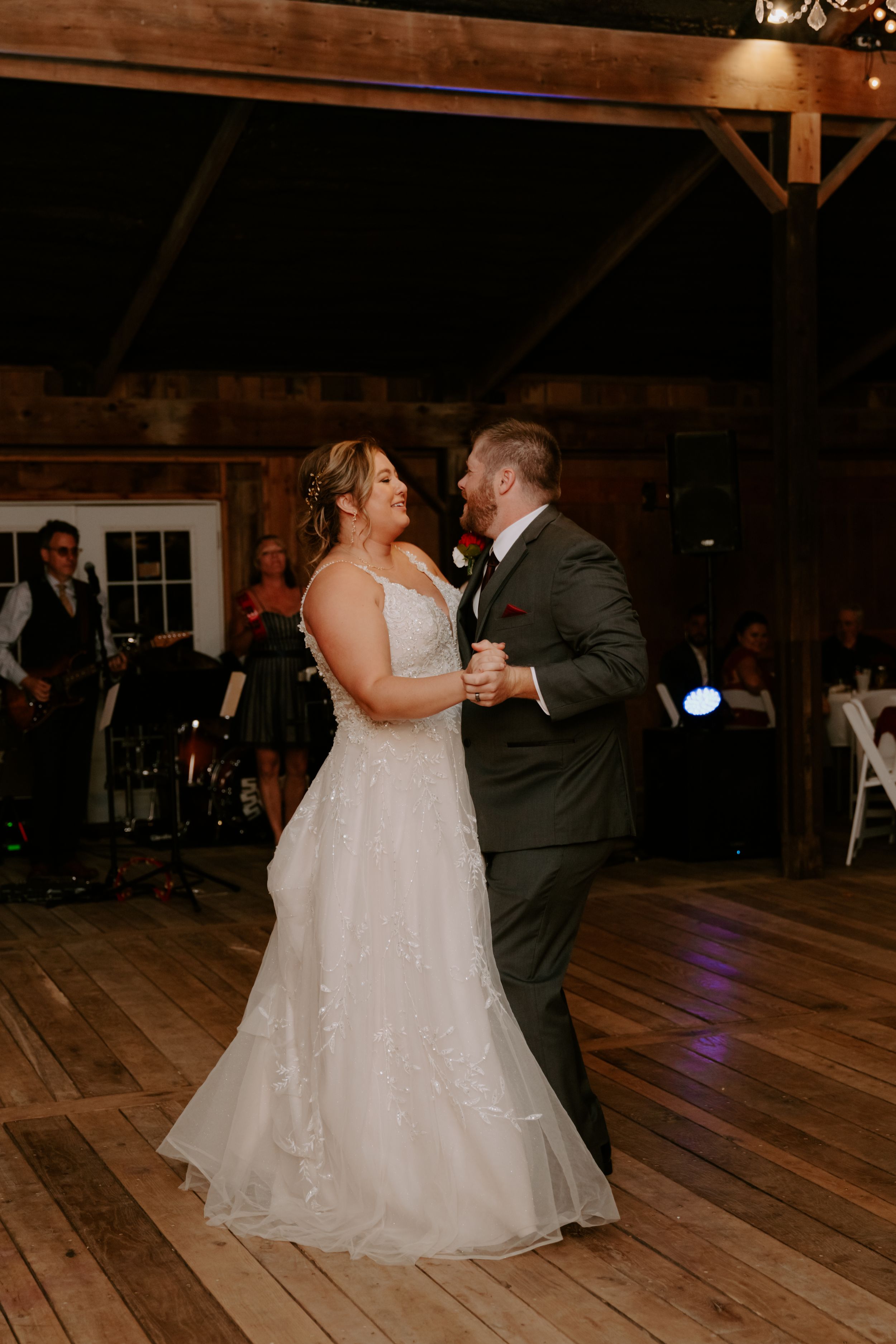 A romantic first dance in a dimly lit rustic barn with wooden floors and ambient lighting.