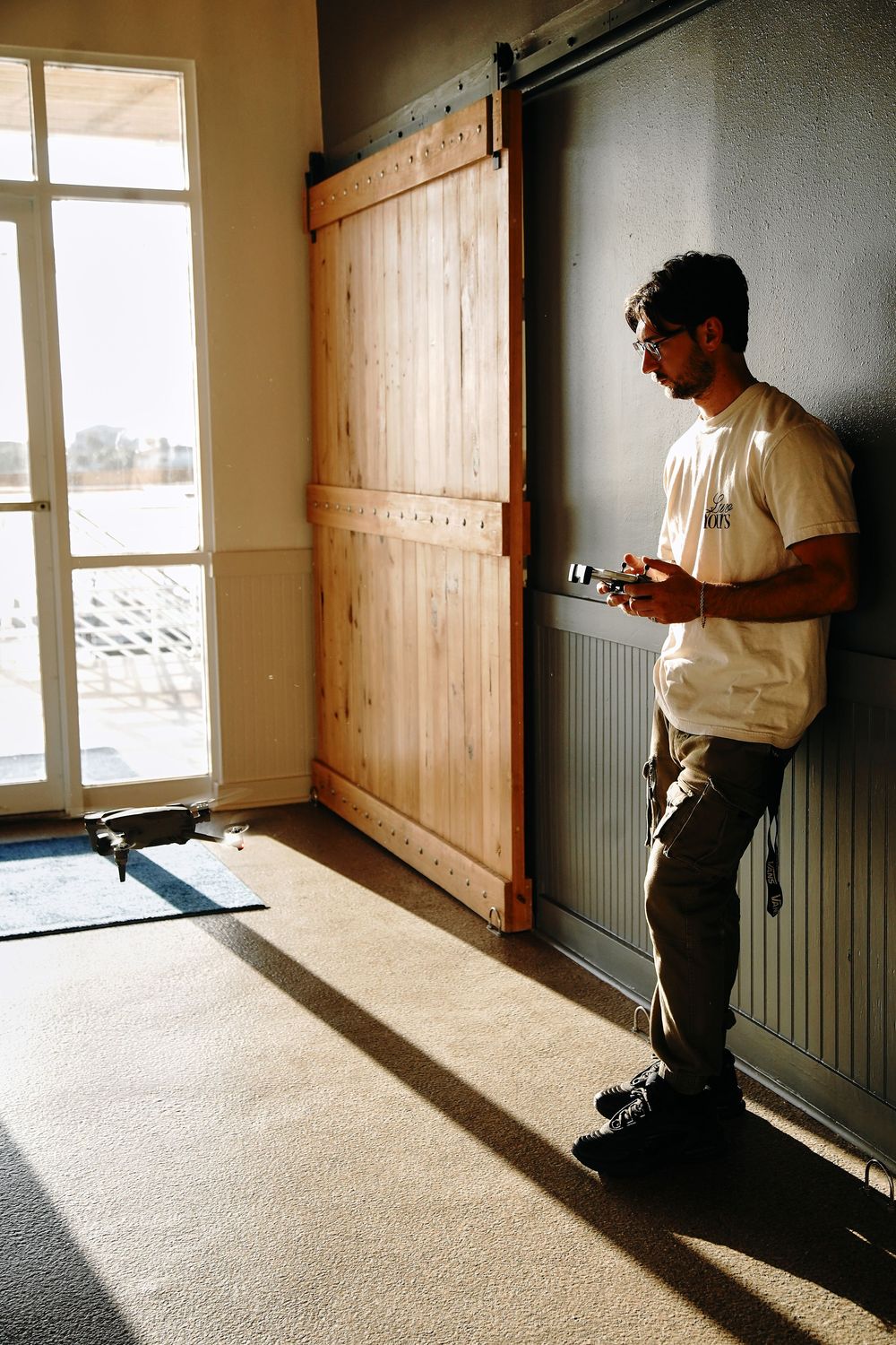 Man leaning against wall next to rustic wooden barn door slider in sunlit interior room.