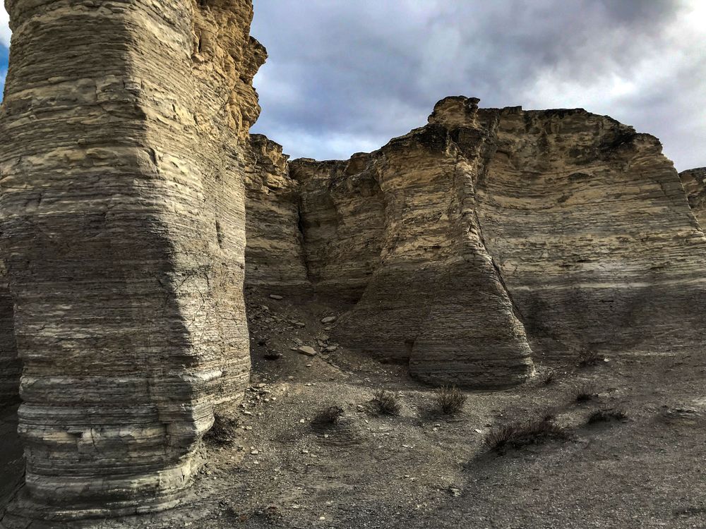 Layered sedimentary rock formations showing erosion patterns under cloudy skies.