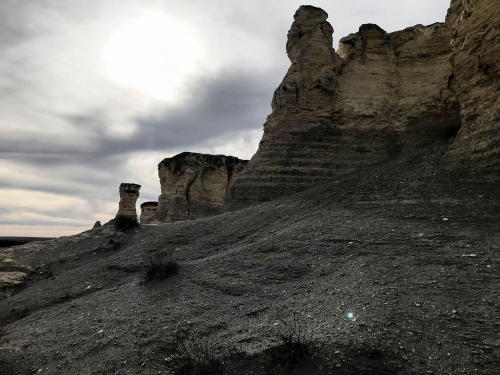 Eroded rock formations rise from barren landscape under dramatic cloudy skies.