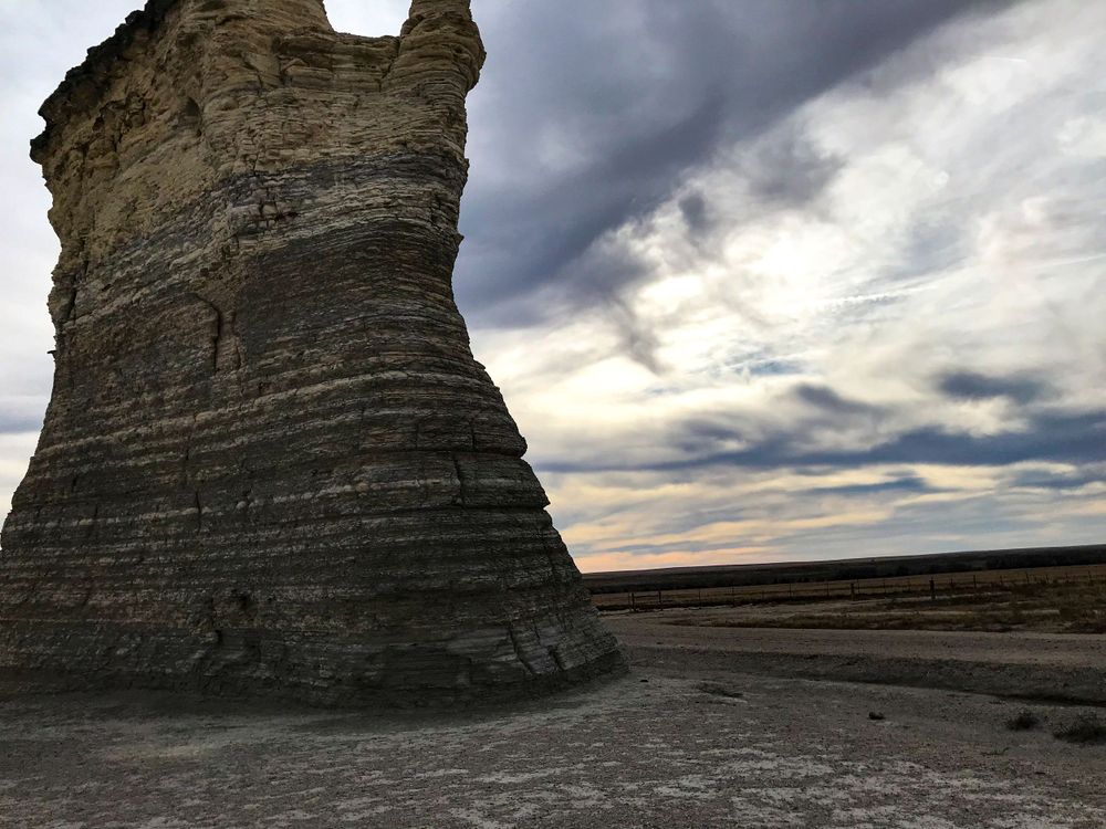 Large limestone pillar formation in Monument Rocks against stormy sunset sky.
