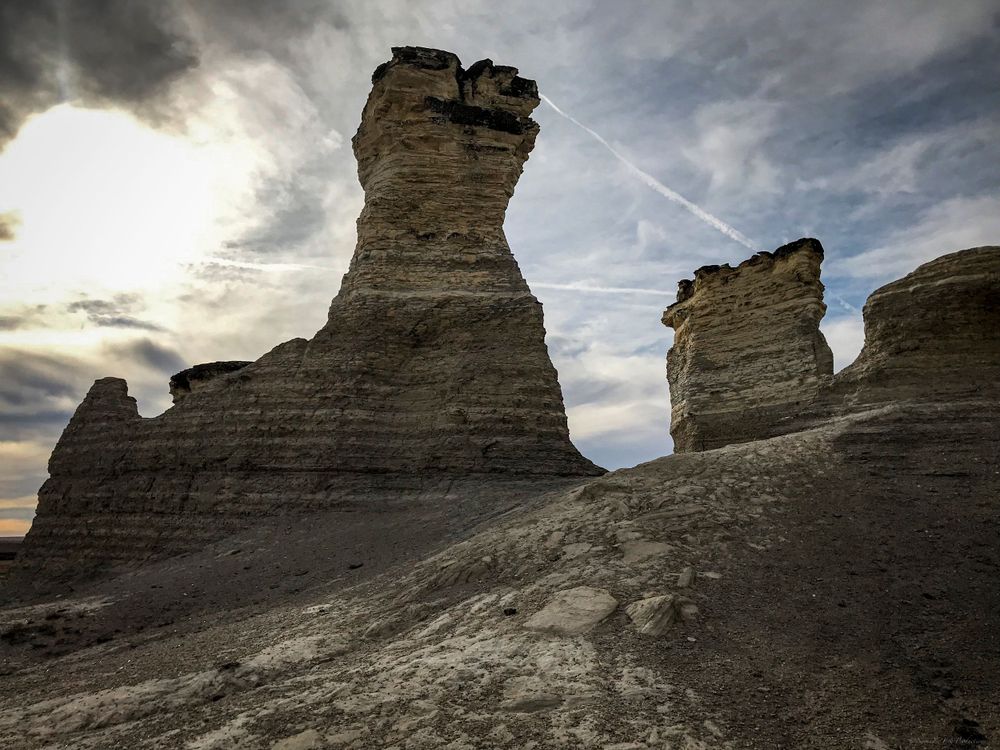 Dramatic rock pillars rise from desert floor with sunburst through stormy clouds.