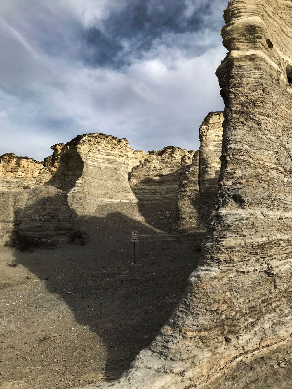 Dramatic limestone rock formations with layered sedimentary patterns cast shadows against a cloudy sky.