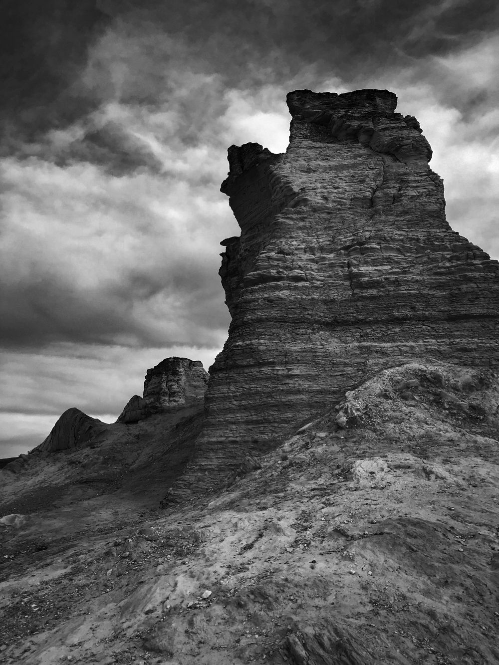Dramatic black and white photograph of an eroded rock formation rising against stormy skies.