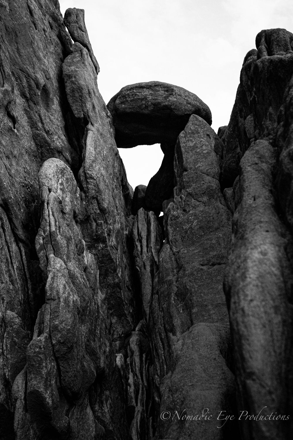 Black and white photograph of a natural stone arch formation between tall rock walls.