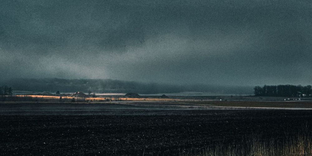 Atmospheric rural landscape with distant lights glowing through fog at dusk.