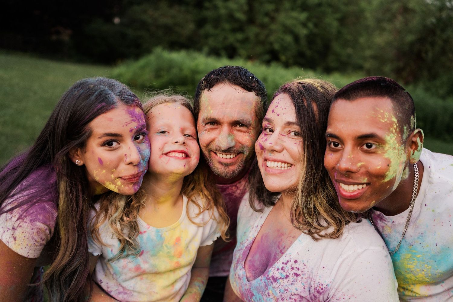 A happy group covered in colorful powder smiles together during a Holi festival celebration outdoors.