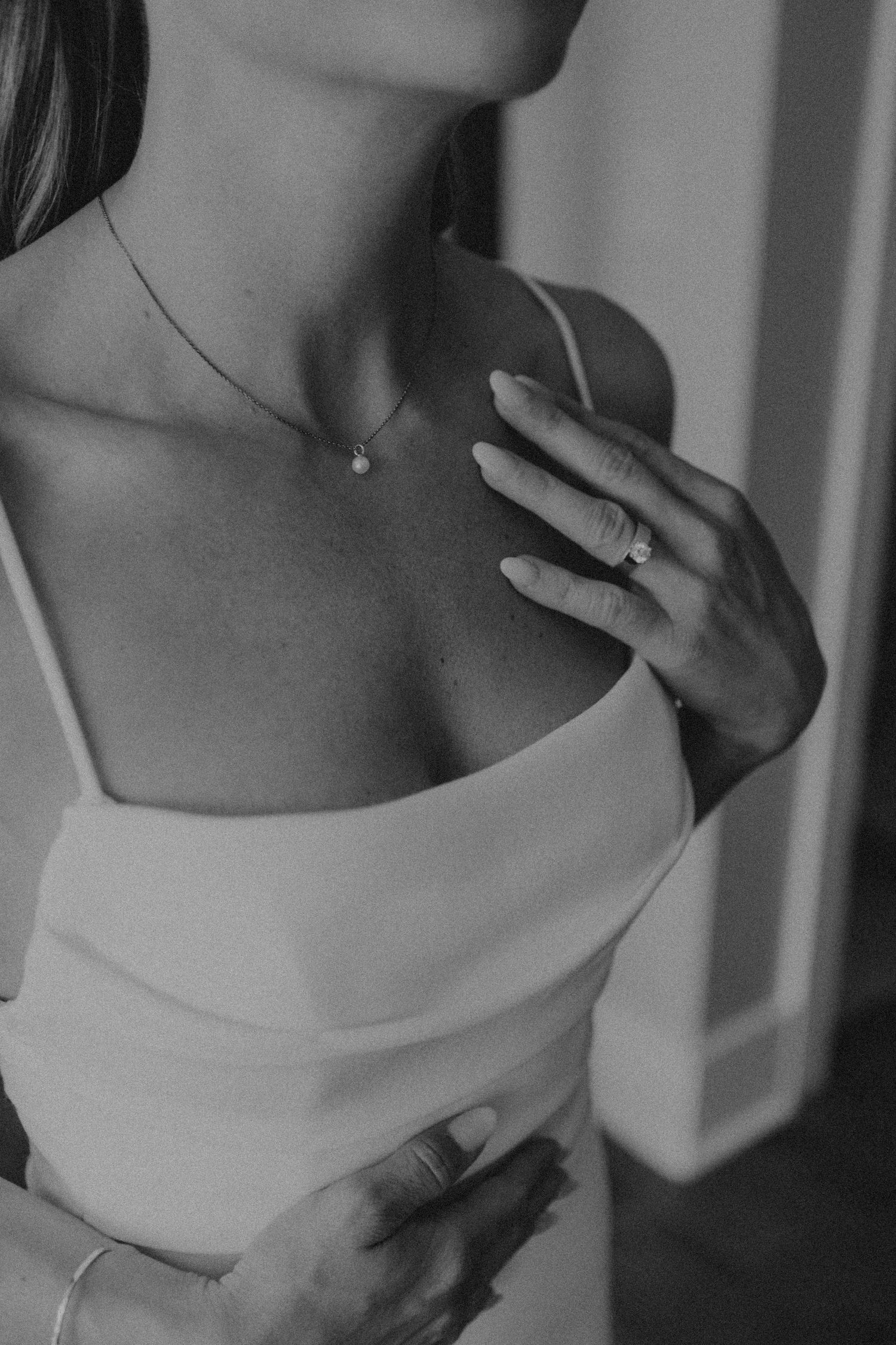 Close-up of delicate jewelry and white dress details in black and white.