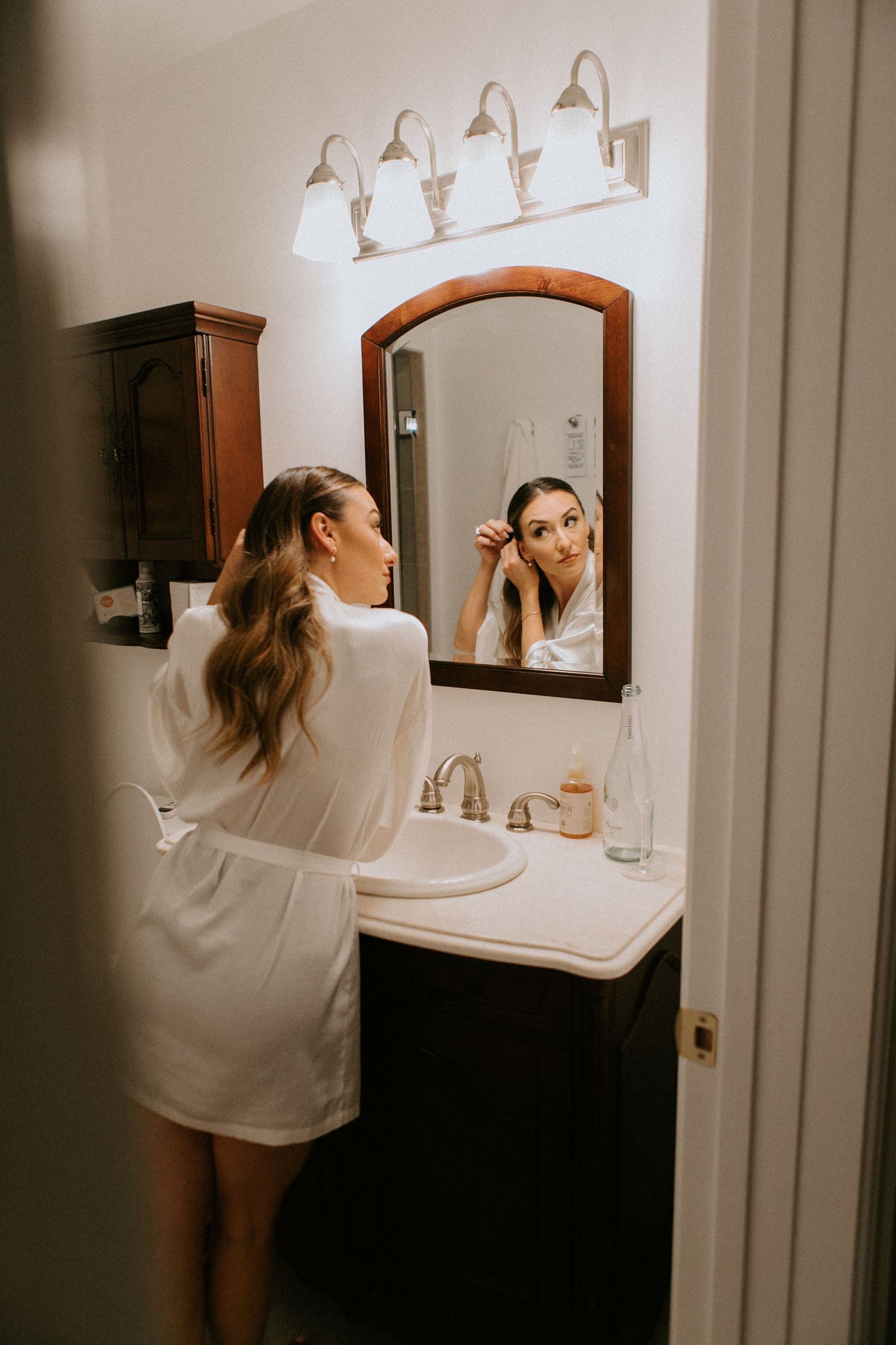 Getting ready scene at bathroom vanity with arched mirror and warm lighting.
