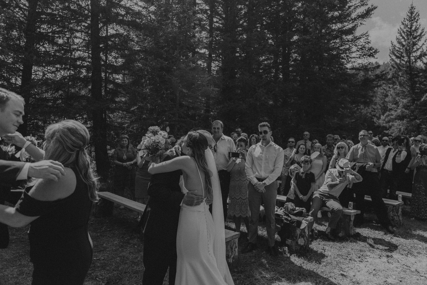Outdoor forest wedding ceremony with guests gathered in black and white.