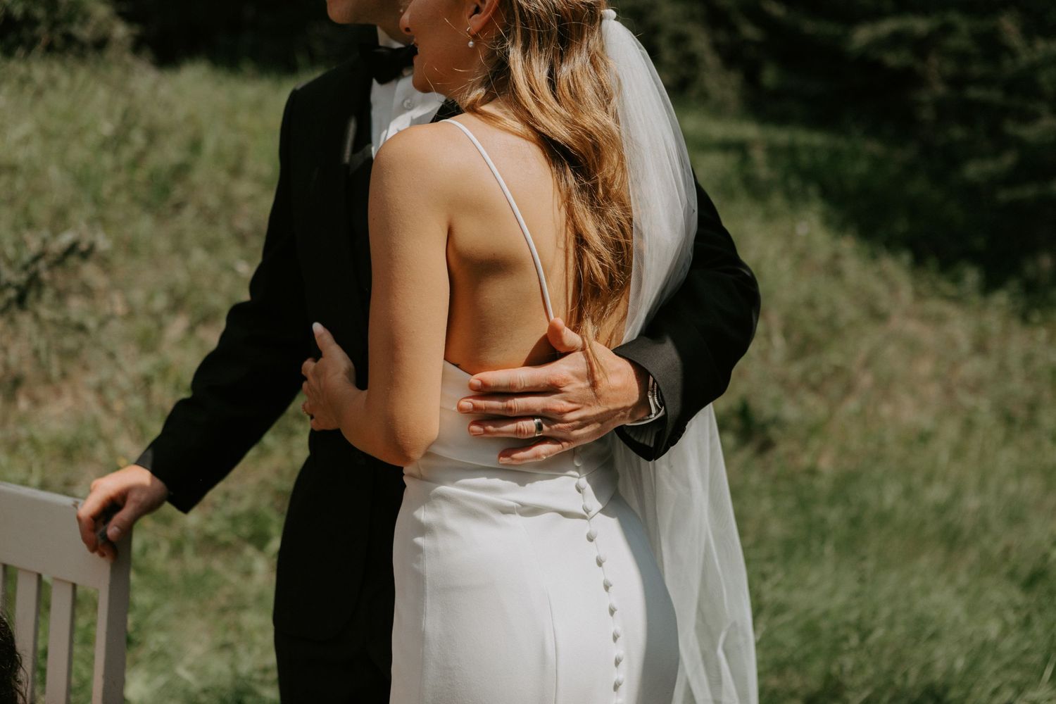 Intimate wedding moment captured in sunlit mountain meadow setting.