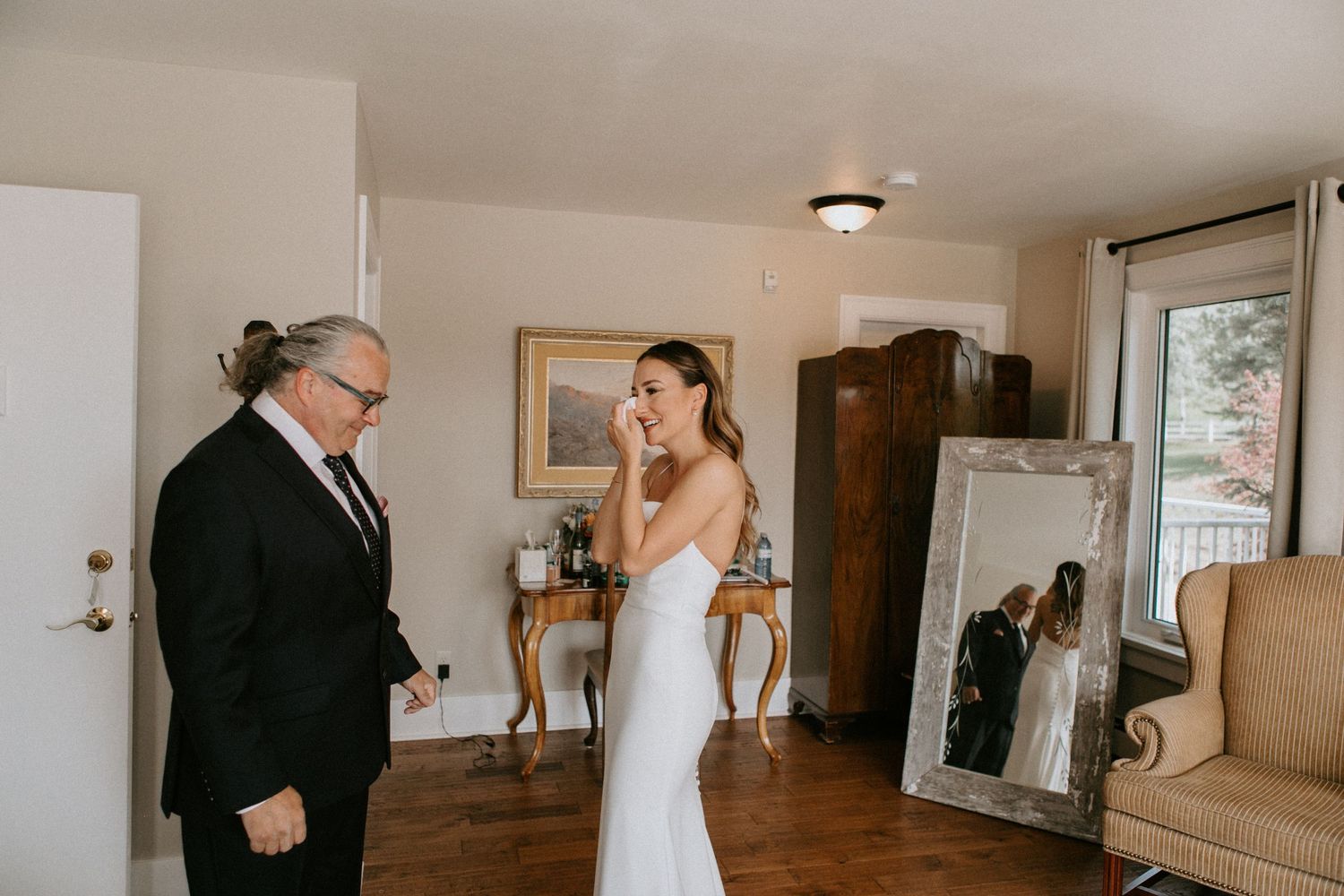 Wedding preparation moment in sunlit room with full-length mirror.