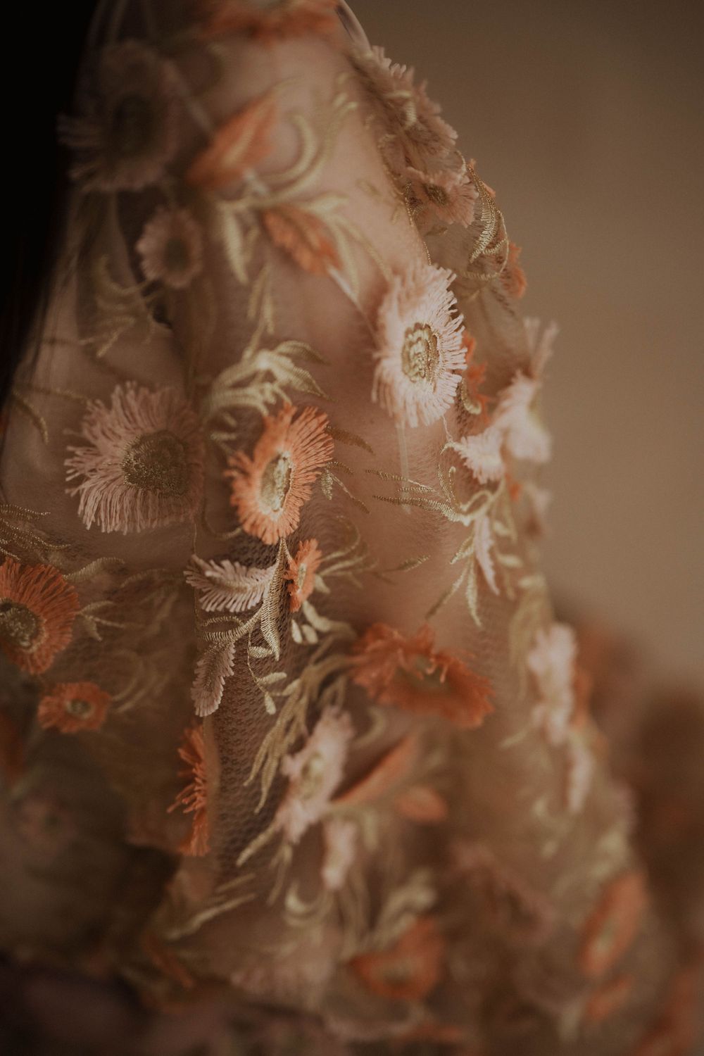 Delicate floral embroidery pattern in peach and cream tones on sheer fabric captured in soft focus.