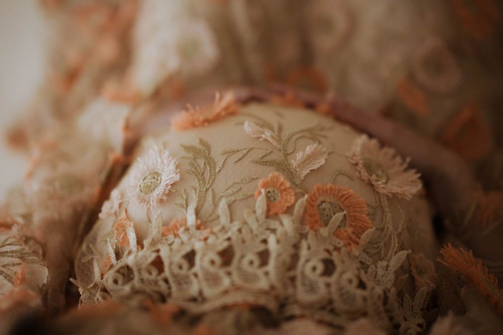 Close-up macro photography of delicate vintage lace fabric with floral embroidery pattern in soft peach tones.