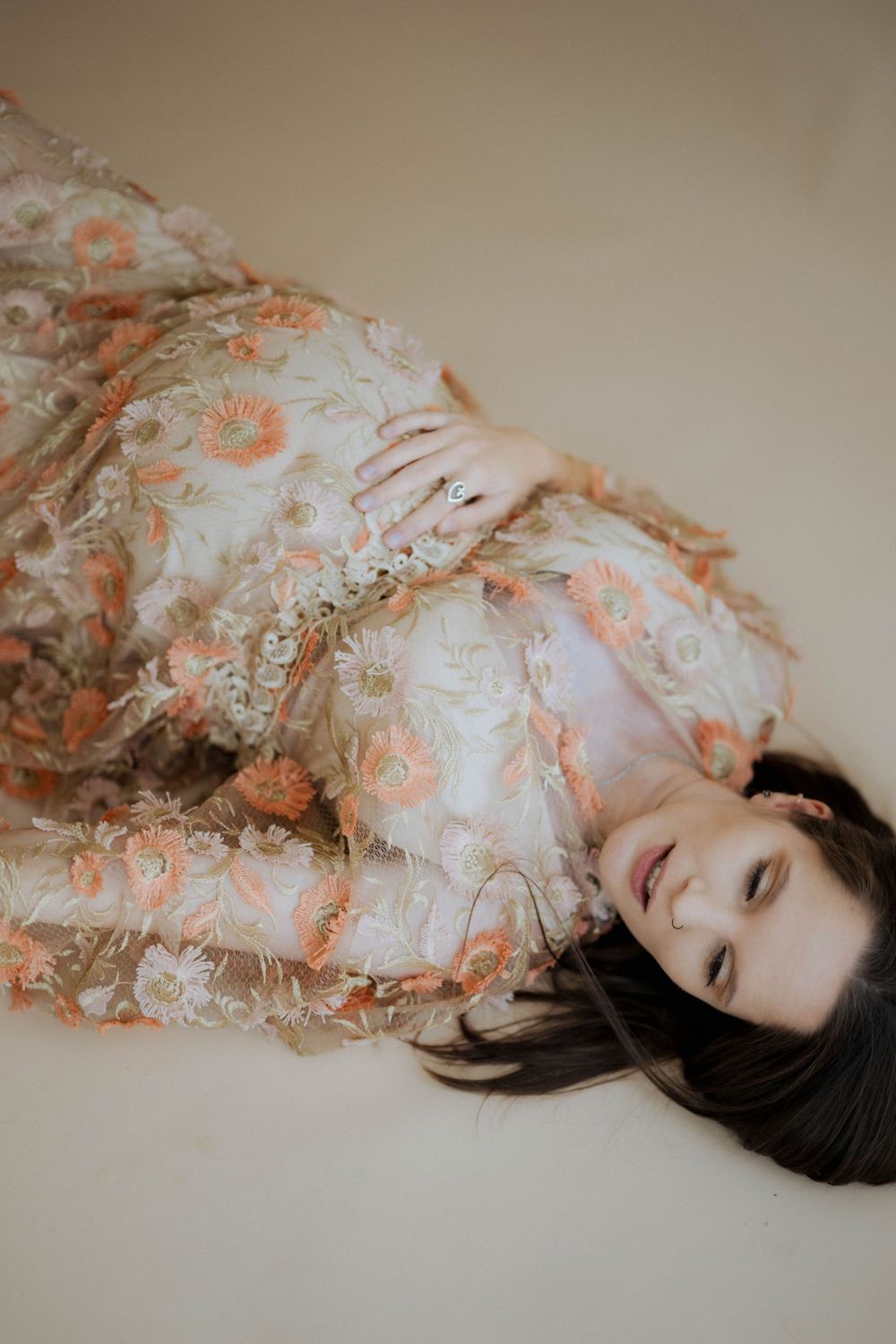 A person lying on a light background wearing a delicate floral dress in peachy pink tones.